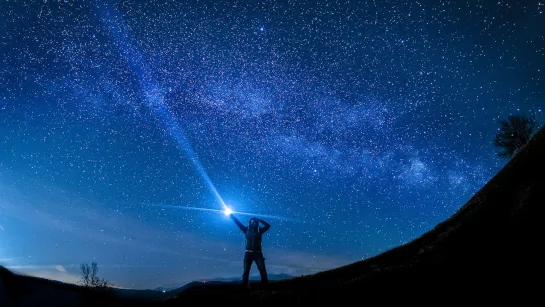 Person hold flashlight into the night sky.